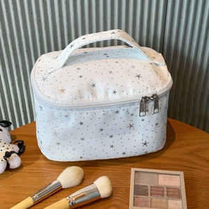 Detail of white canvas makeup bag with silver stars and wide handle on wooden table