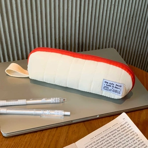 Detail of white quilted pencil case with red zipper and aesthetic typography label