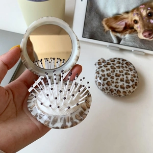 Detail of a leopard print folding hairbrush with integrated mirror and massage bristles