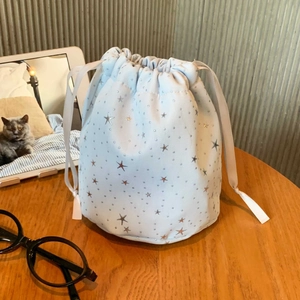 Detail of light blue drawstring pouch with silver stars and fabric texture on wooden desk