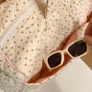 Close-up of quilted floral tote bag showing side pocket holding white sunglasses