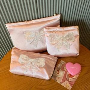 Détail des pochettes en satin rose avec nœuds brodés blancs et tirettes de perles