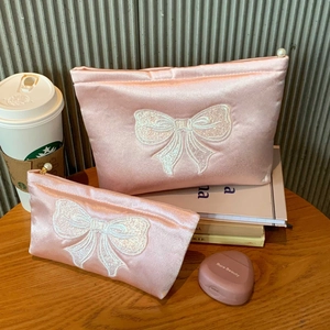 Détail de deux trousses à maquillage en satin rose avec broderie nœud et zip perlé