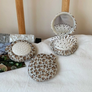 Detail view of foldable leopard print hairbrush with mirror on white fabric