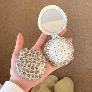 Handheld view of a foldable leopard print hairbrush showing the mirror and cushion bristles