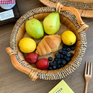 Detail view of a round woven rattan food tray with wooden handles on a dark wood table