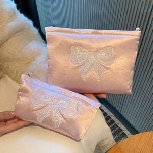 Détail de trousses à maquillage en satin rose avec nœud pailleté et zip en perle