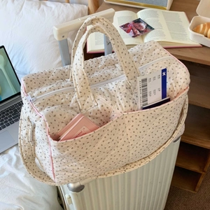 Detail of floral quilted travel tote bag on a suitcase showing pink straps and side pocket