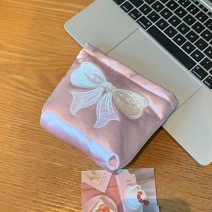 Détail de la trousse à maquillage en satin rose avec broderie nœud blanc et texture perlée