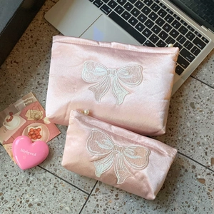 Détail de trousses à maquillage en satin rose avec broderie nœud et fermeture perle
