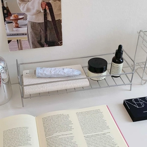 Detail of a minimalist silver wire storage rack with skincare products on a white surface