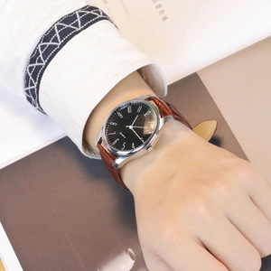 Close-up of a silver men's watch with a black dial and brown leather strap on wrist