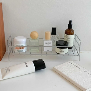 Close-up of a silver stainless steel mesh storage rack for cosmetics on a desk