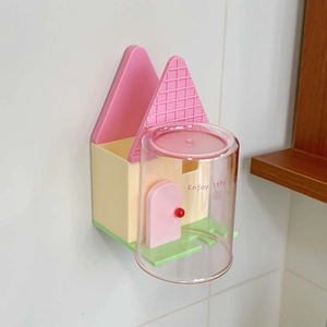 Dettaglio del portaspazzolino a forma di casa rosa con bicchiere Enjoy Life a parete