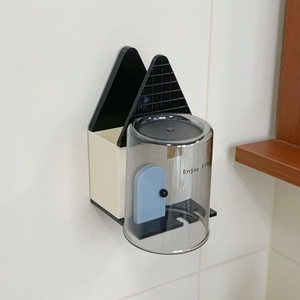 Dettaglio del portaspazzolino a forma di casa e tazza grigia su parete in piastrelle