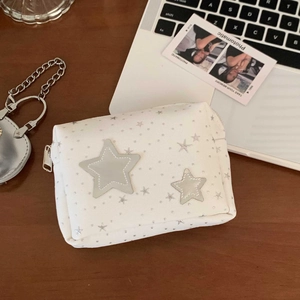 Close-up of a white star-patterned makeup bag with a silver zipper on a wooden desk