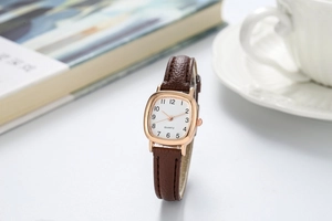 Detailopname van een roségouden vierkant horloge met een bruine lederen horlogeband