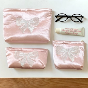 Vue à plat de trousses à maquillage en satin rose de trois tailles avec nœud brodé