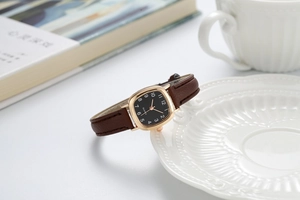 Detail van vierkant quartzhorloge met bruine leren band en zwarte wijzerplaat op bord