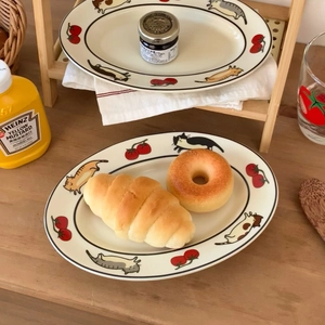 Assiette ovale en céramique décorée de chats et tomates posée sur table en bois