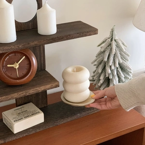 Detail of a creamy white triple-tier ring scented candle held in hand on a wooden shelf