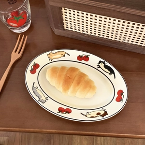 Détail d'une assiette ovale chat et tomate avec un croissant frais sur table en bois