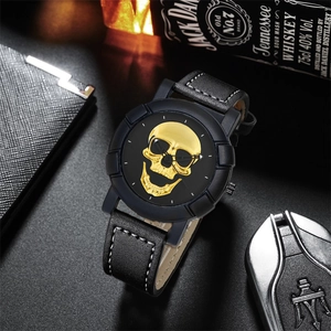 Detail of matte black men's watch featuring a 3D gold skull relief and leather strap