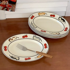 Assiettes ovales en céramique empilées avec motifs de chats et tomates peints sur table en bois