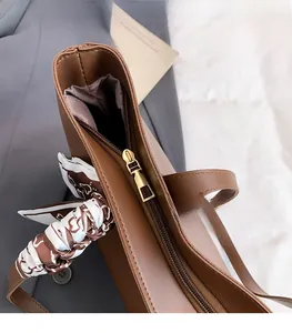 Detailed close-up of brown PU leather tote bag with gold metal zipper and silk scarf handle
