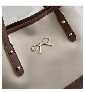 Detail of golden bow logo and premium stitching on beige and brown leather tote bag