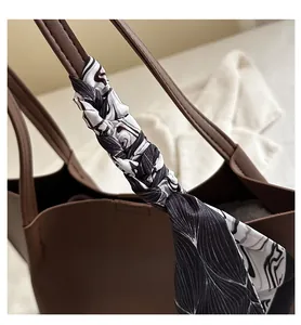 Detail of a brown leather tote bag handle wrapped with a decorative patterned silk scarf