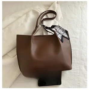 Detail of a brown leather tote bag featuring a floral scarf handle and smartphone size reference