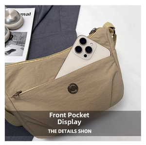 Detailed view of the front zipper pocket on a beige nylon crossbody bag holding a smartphone