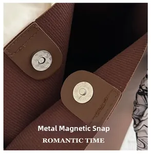 Detail shot of the magnetic hardware buckle and striped lining on this brown shoulder bag