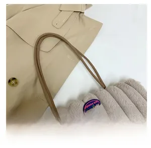 Detail view of plush tote bag with slim leather handles and fashion badge on khaki coat