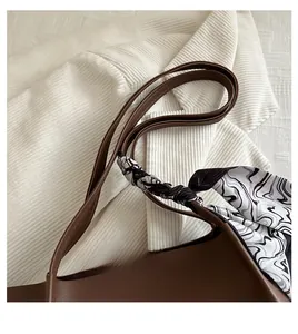 Close-up of brown leather tote bag handle with a stylish black and white silk scarf detail