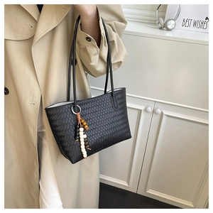 Detail of black woven tote bag with wooden bead charm and slim shoulder strap