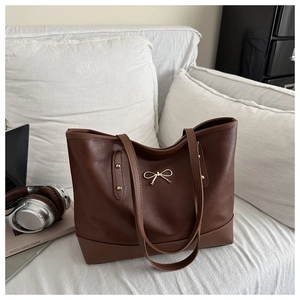 Detail of dark brown tote bag featuring golden bow metal buckle and rivet hardware