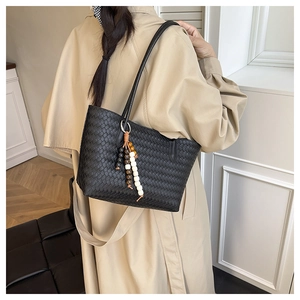 Detail of black woven tote bag with beaded tassel charm on a trench coat model