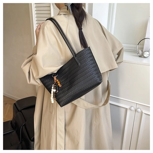 Detail of black woven tote bag with colorful bead tassel on model's shoulder