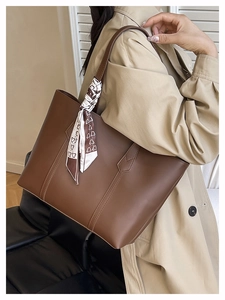 Detail of a brown leather tote bag featuring a white printed silk scarf on the strap
