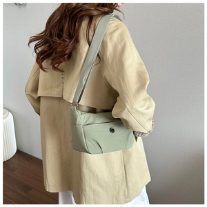 Light green nylon crossbody bag shown from the back on a model wearing a trench coat