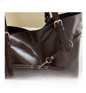 Detailed close-up of dark brown leather tote with golden metallic buckles and hardware