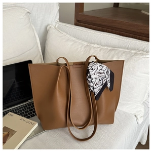 Brown leather tote bag with decorative silk scarf on a desk with a laptop
