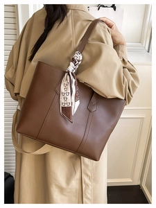 Detail of dark brown leather tote bag with decorative bear silk scarf on handle
