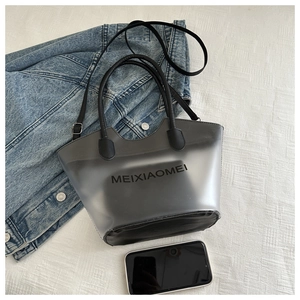 Détail du sac cabas gris en PVC avec logo MEIXIAOMEI et bandoulière noire à côté d'un GSM