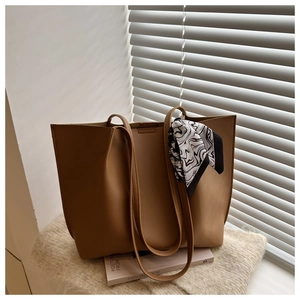 Detailed close-up of brown matte leather tote bag handle featuring a stylish silk scarf