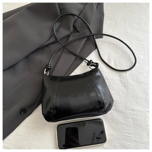 Close-up of black glossy dumpling bag showing smooth texture and size relative to a smartphone