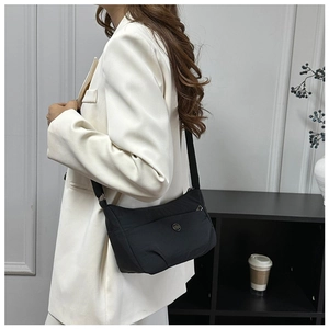 Detail of minimalist black nylon crossbody bag with circular metal logo and wide strap