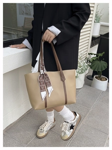 Detail of a beige tote bag featuring brown straps and a decorative patterned silk scarf